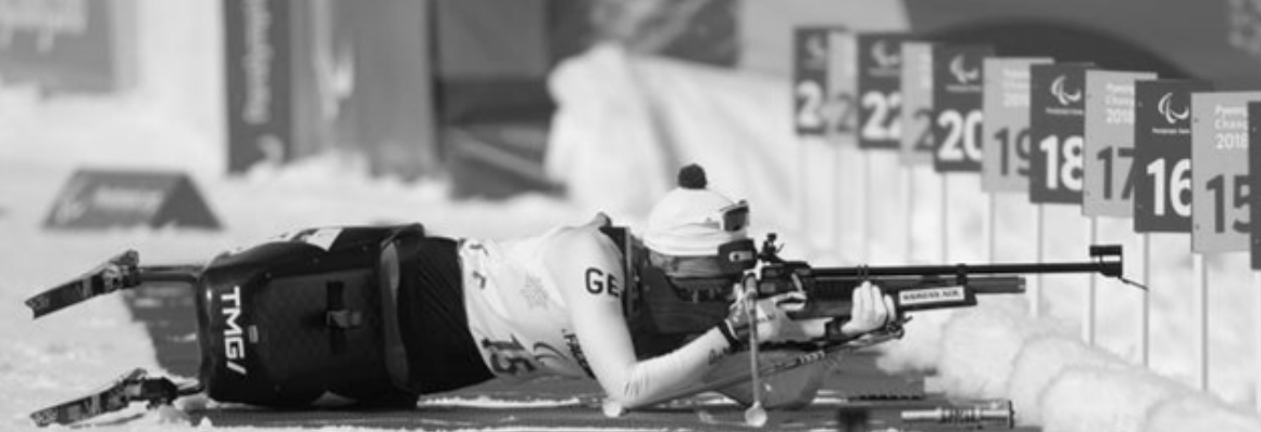 Biathletin liegt im Schnee und zielt mit Gewehr auf Zielscheiben